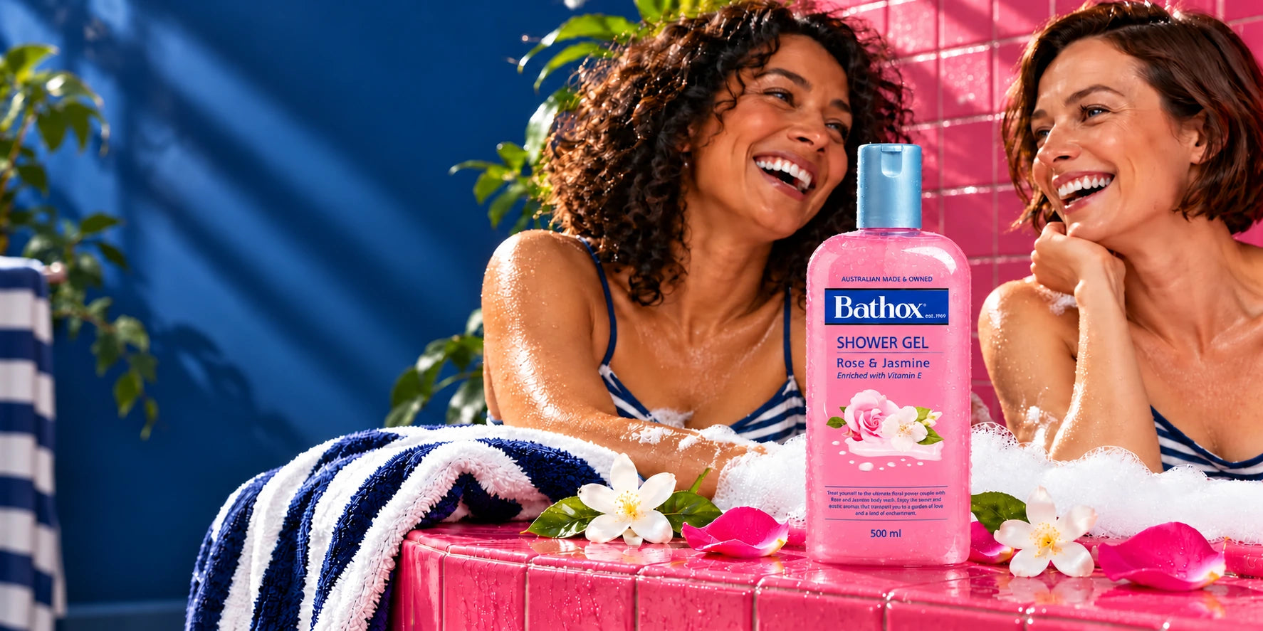 Rose & Jasmine with two smiling women, pink tiles, bubbles and blue striped towels.